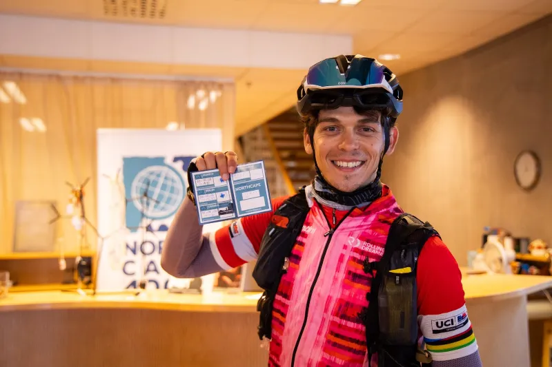 A smiling rider in a helmet shows his stamped carnet at the gate in Gränna