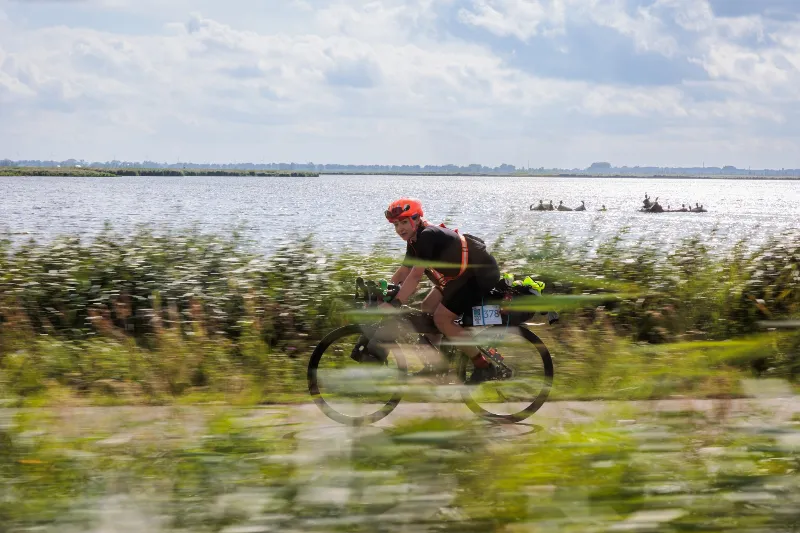 A rider with bikepacking bags passing fast through tall grass, a lake in the background